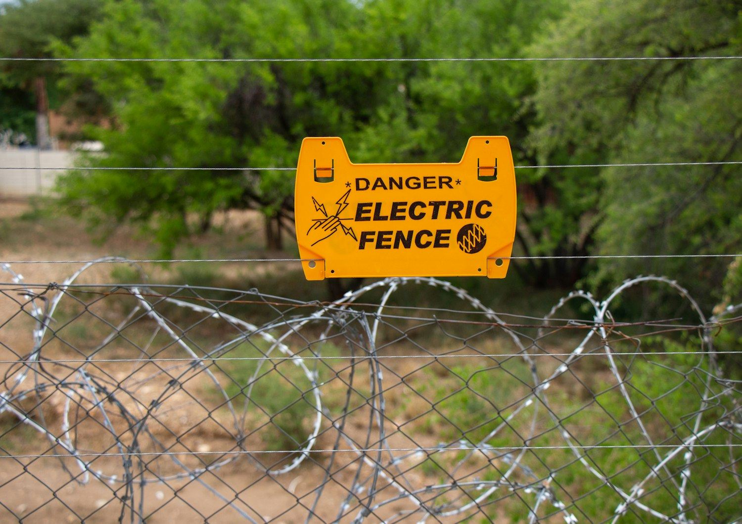 An electric fence warning sign on a perimeter security fence